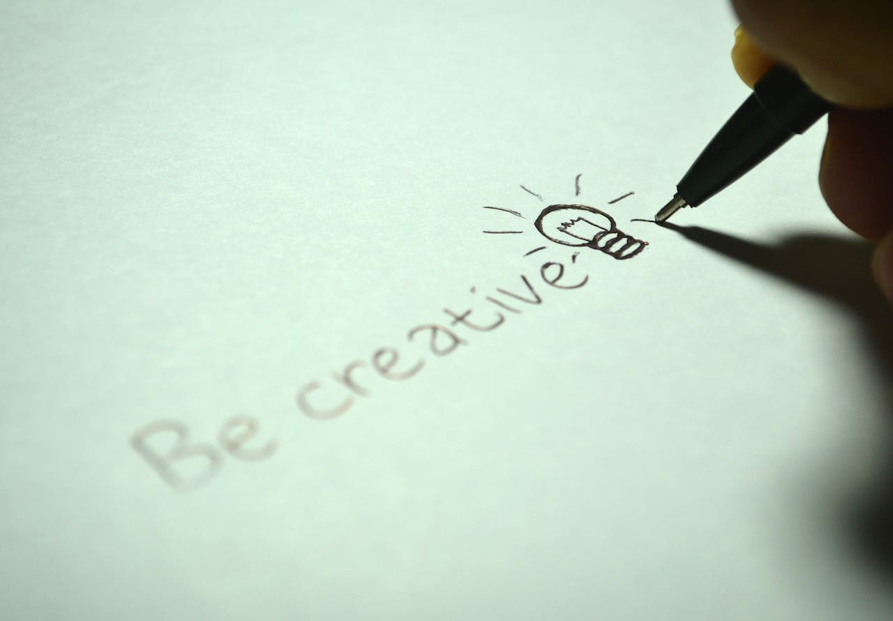 Close-up of handwritten Be creative with a light bulb sketch on paper.
